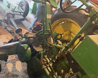 Vintage John Deere Model B tractor  A classic piece of agricultural machinery manufactured between 1935 and 1952.   John Deere B with a large exposed flywheel on the side. Equipped with a manual transmission and a power take-off (PTO) shaft for running implements. Gated gear shifter, heavy-duty metal pedals, and traditional mechanical controls with a distinctive two-cylinder design.