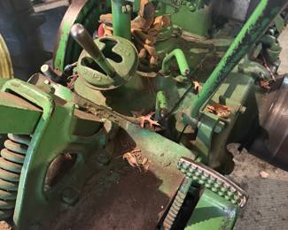 Vintage John Deere Model B tractor  A classic piece of agricultural machinery manufactured between 1935 and 1952.   John Deere B with a large exposed flywheel on the side. Equipped with a manual transmission and a power take-off (PTO) shaft for running implements. Gated gear shifter, heavy-duty metal pedals, and traditional mechanical controls with a distinctive two-cylinder design.