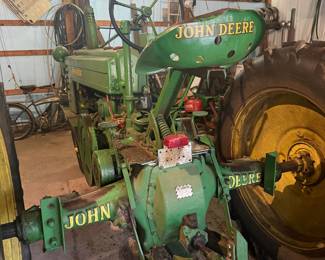 Vintage John Deere Model B tractor  A classic piece of agricultural machinery manufactured between 1935 and 1952.   John Deere B with a large exposed flywheel on the side. Equipped with a manual transmission and a power take-off (PTO) shaft for running implements. Gated gear shifter, heavy-duty metal pedals, and traditional mechanical controls with a distinctive two-cylinder design.