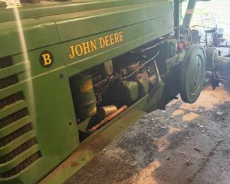 Vintage John Deere Model B tractor  A classic piece of agricultural machinery manufactured between 1935 and 1952.   John Deere B with a large exposed flywheel on the side. Equipped with a manual transmission and a power take-off (PTO) shaft for running implements. Gated gear shifter, heavy-duty metal pedals, and traditional mechanical controls with a distinctive two-cylinder design.