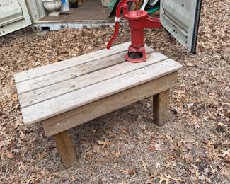  vintage-style red hand water pump mounted on a rustic wooden bench,
