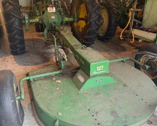 John Deere 127 rotary mower, also referred to as a gyro mower.  It is designed for cutting brush, weeds, and tall grass.  The mower features a durable metal deck and is designed to attach to a tractor.  These mowers are typically used for clearing pastures and maintaining roadsides. 