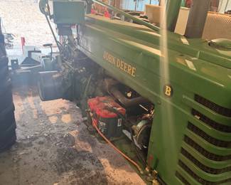 Vintage John Deere Model B tractor  A classic piece of agricultural machinery manufactured between 1935 and 1952.   John Deere B with a large exposed flywheel on the side. Equipped with a manual transmission and a power take-off (PTO) shaft for running implements. Gated gear shifter, heavy-duty metal pedals, and traditional mechanical controls with a distinctive two-cylinder design.