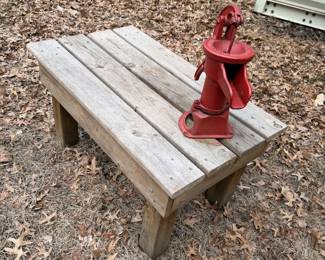  vintage-style red hand water pump mounted on a rustic wooden bench,
