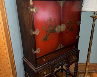 antique red lacquered Chinoiserie cabinet from the 1920s or 1930s. It features hand-painted Asian-inspired scenes and brass on a Jacobean-style carved stand $800