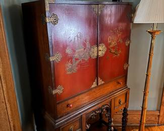 antique red lacquered Chinoiserie cabinet from the 1920s or 1930s. It features hand-painted Asian-inspired scenes and brass on a Jacobean-style carved stand $800
