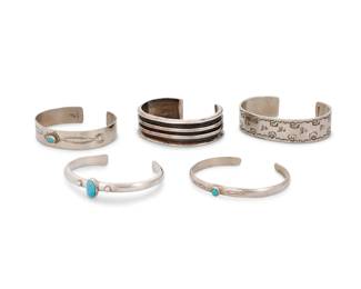 203
A group of Southwest style silver cuff bracelets
Mid/late 20th century
Five works:

Edward Platero (b. 1972, Laguna Pueblo/Diné)
Late 20th/21st century
Stamped: EP [with bird track picto]
A narrow cuff with small set turquoise cabochon and stamp work details
6.4" total inner C x 0.25" H, with a 1" gap

A group of Southwest style cuffs
One with etched mark: Tseu / .925 / [cipher]
Comprising a chunky ridged sterling silver cuff and a narrow sterling silver cuff with set turquoise, together with two nickel silver cuffs, each with stamp work motifs, and one with set turquoise
4 pieces
Largest: 7" total inner C x 0.625" H, with a 1.125" gap; Smallest: 6.25" total inner C x 0.75" H, with a 1.25" gap

5 pieces total
Sterling: 82.9 grams gross
Estimate: $200 - $400