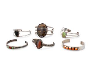 259
A group of Southwest style silver cuff bracelets
Mid/late 20th century
Four marked for sterling; two further marked for maker: Don Lucas / [sun picto]
Comprising three wire cuff bracelets, each with single set stones including tiger iron, turquoise, and onyx, as well as three narrow single band cuffs, one with row-set coral and turquoise and one with row-set spiny oyster and one with a set cabochon of petrified wood
6 pieces
Largest: 6.625" total inner C x 1.125" H; Smallest: 6.125" total inner C x 1.875" H
143.5 grams gross
Estimate: $200 - $400