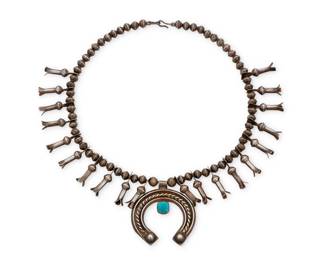 161
A diminutive Southwest silver and turquoise squash blossom necklace
Early/mid-20th century
Unmarked
A single strand of silver pearls with twenty blossoms suspending a twisted wire and stone set naja
17.25 x 1.875" H
57.9 grams gross
Estimate: $600 - $800