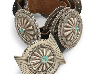 84
A Joe H. Quintana Cochiti sterling silver and turquoise concho belt
Joe H. Quintana (1915-1991, Cochiti Pueblo)
Mid/late 20th century
Buckle stamped with artist's cypher: JHQ
A chunky belt in cast sterling silver and stamp work, with a butterfly concho bow-shaped buckle with central set turquoise and repoussé rosette motif, and eight matching oval conchos, each set with a central turquoise stone and all mounted to a wide black leather strap
Buckle: 3" H x 3.75" W; Each concho: 3" H x 3.5" W; Belt: 36.25" L x 1.5" H
644.0 grams gross
Estimate: $1,500 - $2,500