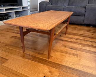 Teak Coffee Table by Kristensen & Thomassen. This Mid-Century Modern coffee table features classic clean lines, tapered legs, and a warm wood finish, embodying the timeless appeal of MCM design. The table includes a woven lower shelf, adding both visual interest and practical storage—an iconic detail found in many Danish-inspired mid-century pieces.