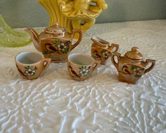 Charming assorted vintage decorative objects collection featuring a polished brass candelabra, a miniature ceramic tea set, a yellow glass shoe figurine, and several additional novelty and figural décor pieces.
