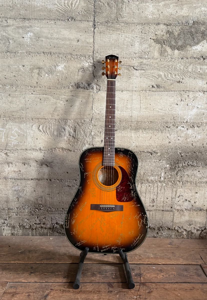 This lot features a Fender DG-22S acoustic guitar and case. This guitar comes signed by various artists and bands. The Fender DG-22S is a highly-regarded, 1990s-era Korean-made dreadnought acoustic guitar, often praised for its high value, solid spruce top, and striking exotic back/side wood options (flamed maple, bubinga, or asian striped ebony). It features a glossy, 20-fret nato neck, rosewood fingerboard, and gold die-cast tuners.

