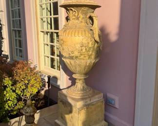 English amphora-form lidded garden urn made of stone or composite stone, featuring extensive decoration with vine leaves and grapes, and standing on a square pedestal base.