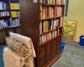Double sided cabinet filled with books, vintage blanket holder with sheepskin rugs, and hand, crocheted blanket