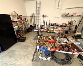 Garage full of various hand tools, gardening items, wheel barrow, Whirlpool refrigerator/freezer, misc.
