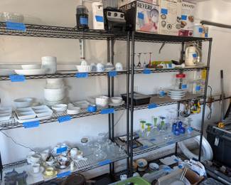 Massive Dishware Selection: Heavy-duty wire shelving loaded with a huge assortment of clean, versatile white dishware, including dinner plates, bowls, square plates, and divided serving platters.

Teacups & Saucers: A beautiful collection of teacups and saucers, featuring classic white sets as well as delicate, vintage-style floral patterns.

Colorful & Vintage Glassware: Eye-catching stemware collections including vibrant cobalt blue goblets, bright green-stemmed glasses, tall multicolored stemware, and plenty of everyday clear drinking glasses and mugs.

Small Kitchen Appliances & Gadgets: Features boxed appliances including a Crock-Pot and an Automatic Rice Cake & Dough Maker, plus blenders, an electric can opener, an immersion blender, a food scale, and glass storage jars.