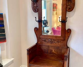 Antique oak hall tree with a beveled mirror with  carved scroll work, four coat hooks and a lift seat  for storage