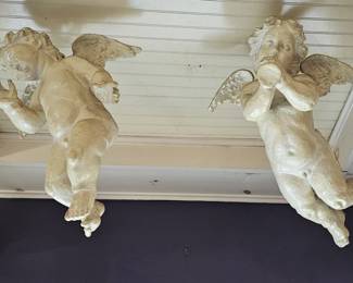 Pair of life-sized playful winged cherub sculptures in an off-white finish.