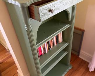 vintage-style wooden bookcase features a painted green finish, an arched top shelf, fluted columns, and a small drawer with decorative knobs. 