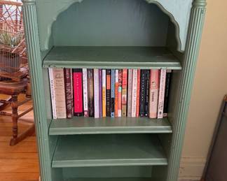 vintage-style wooden bookcase features a painted green finish, an arched top shelf, fluted columns, and a small drawer with decorative knobs. 