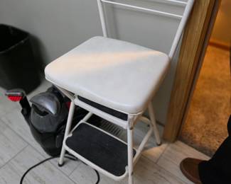 This vintage white metal item is a Cosco Kitchen Step Stool Chair, which features a lift-up seat to function as both a seat and a step ladder. 