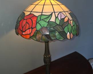 Tiffany style table lamp featuring a handcrafted stained glass shade with a red rose and greenery motif, a design commonly found in lighting by brands like Amora Lighting. 