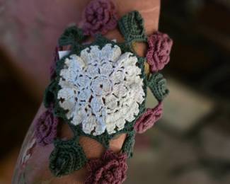 This vintage-style handmade crochet item appears to be a decorative floral appliqué or doily featuring a central white flower surrounded by rose buds and leaves. 
