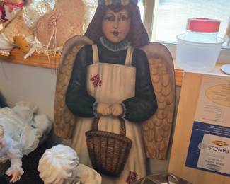 This image features a vintage, handcrafted Christmas decoration depicting a Dickens-style girl angel carrying a basket. It is part of a festive display that also includes various other figurines and holiday decor. 