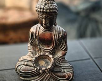 This item is a decorative seated Buddha statue that doubles as a votive or tea light candle holder. 