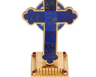 120 Cartier: A 14K Gold, Lapis Lazuli and Ruby Cross Of a cross design featuring panels of carved lapis lazuli, set upon a tiered square fluted gold mount accented by four round ruby cabochons, inscribed on the back "Whosoever therefore shall confess Me before men, him will I confess also before my Father which is in Heaven, Matthew 10:32" and "Nov-Dec 1948, to Clare from Harry," signed Cartier  Measures: 4 x 1 5/8 x 1 5/8 in. 144.2 grams gross Estimate: $10,000 - $15,000