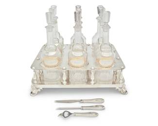 212 An Armand Frenais silver plated spirits bottle holder and glass bottles Late 19th/early 20th century; France Holder marked: A. Frenais / BLANC70 / AF [anchor cipher] / 70; each tag marked: Sterling / R / B [with sword through the letter] / Co; each bar utensil marked indecipherably, likely same maker as tags Comprising a fitted holder raised on grapevine-form feet, housing nine glass bottles with painted and gilt labels for various spirits, together with seven later R. Blackington & Co. sterling silver liquor tags, a bottle opener, a bar knife, and an ice pick, utensils monogrammed Overall: 14.75" H x 18.25" W x 14.75" D; Each bottle: 12.375" H x 3.5" Dia.; Holder: 5.5" H Tags weight: 2.1 oz. troy approximately Estimate: $600 - $800