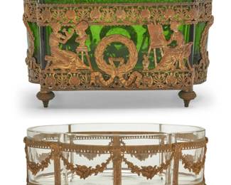 427 Two French gilt metal mounted glass table jardinières Late 19th/early 20th century Comprising one with green glass insert and openwork metal depicting students of the classical arts and laurel wreaths, and another with clear glass insert mounted with swags and paw feet 2 pieces Green: 5" H x 8" W x 4.25" D; Clear: 3.75" H x 9.75" W x 6.25" D Estimate: $200 - $300