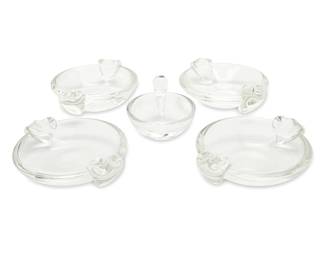 346 A set of four Steuben glass ashtrays and an olive dish Two works:  A set of four ashtrays, model 7836, mid-20th century Designed 1936 by George Thompson (1913-1981) Etched: Steuben Each: 2.27" H x 8.75" W x 7.375" D approximately 4 pieces  A scroll handle olive dish, model 7857, late 20th/early 21st century Designed 1939 by John Dreves (1913-2003) Etched: Steuben With original box Dish: 3.75" H x 6.125" W x 5" D; Box: 6.25" H x 9.375" W x 6.375" D  5 pieces total Estimate: $250 - $350