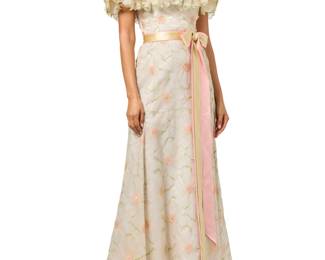 148 Arnold Scaasi: An Embroidered Floral Silk Organza Gown Circa 1970s-1980s Label: Arnold Scaasi A long sleeveless dress of glazed organza fabric flowers, attached and embellished with pink and green embroidery, with a fitted lightly boned silk-lined bodice with a deep ruffled flower collar, and a long flared skirt with a partially detachable pink and green satin ribbon bow belt, the skirt with a double lining of organza and white silk, with back zip closure  No size label: bust across front: 18 in.; Waist: 13 1/2 in.; hips: 18 1/2 in.; CB length: 50 in. Estimate: $200 - $400