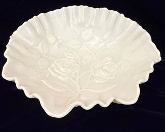 A vintage white milk glass bowl by Imperial Glass, featuring an embossed "American Beauty" rose pattern with leaves. The rim is scalloped and ruffled, with a crimped edge. The bowl has a satin finish and sits on a low pedestal base. This piece is characteristic of mid-century American glassware, often used as a rose bowl or decorative centerpiece.