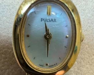 This lot features two women's wristwatches: a gold-tone Pulsar with a mother-of-pearl dial and a silver-tone Caravelle with a white dial. The Pulsar watch has an oval case and a multi-link bracelet, with 'PULSAR', 'WATER RESISTANT', 'ST. STEEL', '1N00-X139 R2', 'MOVEMENT JAPAN', and '500106' visible on the case back. The Caravelle watch has a round case, Roman numerals, and a metal expansion band, with 'CARAVELLE', 'WATER RESISTANT', and 'T SWISS T' visible on the dial. Both appear to be quartz-powered and show signs of wear consistent with age and use.