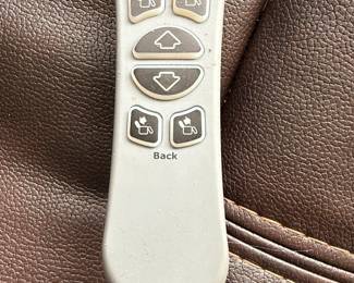 This is a brown, faux leather power lift recliner chair. It features plush, overstuffed cushioning with decorative stitching in a contrasting cream color. The chair is operated by a wired remote control that allows for adjustment of the headrest and back, as well as a lift function, indicated by directional arrows on the remote. The remote also has buttons for headrest and back adjustments, suggesting multiple reclining positions and lumbar support options. The material appears to be a durable, easy-to-clean faux leather, suitable for everyday use. The overall design is contemporary and emphasizes comfort and ease of use, particularly for individuals who may require assistance with standing or sitting.