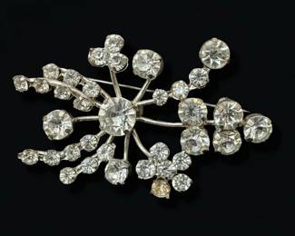 This set features two distinct vintage brooches, both likely dating from the mid-20th century. The larger brooch showcases a bouquet design with three lustrous faux pearls nestled among swirling, pave-set rhinestones that mimic the sparkle of diamonds. Its silver-tone metal setting is intricately detailed, with flowing ribbons and leaf-like elements. The second brooch is a starburst or snowflake design, radiating from a central, larger rhinestone, with smaller stones and clear crystals forming delicate branches. The reverse of the starburst brooch clearly indicates 'MADE IN AUSTRIA', a mark associated with high-quality costume jewelry production from that region. Both pieces are crafted from silver-tone metal, likely a base metal alloy, and are adorned with prong-set rhinestones and faux pearls. The overall aesthetic leans towards Art Deco or Mid-Century Modern styles, popular during their likely period of creation.