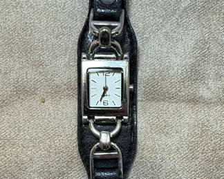 This is a women's quartz wristwatch featuring a square, silver-tone case with a white dial. The dial has simple black hour markers and hands, with 'QUARTZ' printed below the 12 o'clock position. The watch is attached to a black leather cuff-style band, secured with a buckle closure. The band has decorative silver-tone metal accents that connect to the watch case. The case back is stainless steel and bears markings indicating 'WATCH CORP. JAPAN MOVT.' and 'T460'. The overall style is casual and somewhat contemporary, suitable for everyday wear.