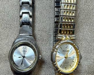This lot contains two women's quartz wristwatches. The first is a Lorus watch with a silver-tone dial, silver-tone metal band, and a stainless steel caseback. It features a simple dial with hour markers and Arabic numerals at 12 and 6 o'clock. The second is a Milan watch with a champagne-colored dial, gold-tone bezel, and a two-tone metal band. It is marked as 'DIAMOND QUARTZ' and has a stainless steel back with a base metal bezel. Both watches appear to be functional quartz movements, suitable for everyday wear.