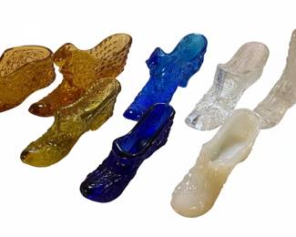 A collection of glass "Cinderella" slipper figurines, also known as "boot" or "shoe" vases, featuring the Daisy and Button pattern. These decorative items are often made from pressed glass and typically feature intricate patterns inspired by historical footwear. The Daisy and Button pattern, characterized by its geometric, textured design, is clearly visible on many of the pieces. They are commonly found in various colors, including the emerald green, amber, yellow, blue, and clear glass seen in the provided images. The design often includes a heel and a pointed toe, with an opening at the top suitable for holding small floral arrangements or serving as a standalone decorative piece. Their appeal lies in their whimsical design and the variety of colors and glassmaking techniques used, particularly the prominent Daisy and Button motif.
