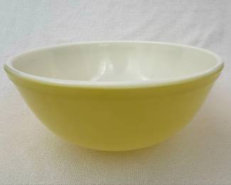 This is a vintage Pyrex mixing bowl in the "Primary Yellow" color, likely from the mid-20th century. It features a classic shape with a solid, bright yellow exterior and a creamy white interior. The bowl is made of durable, opaque Pyrex glass, known for its resistance to staining, chipping, and scratching. The base of the bowl displays the embossed Pyrex logo, indicating its authenticity as a product of Corning Glass Works. This particular yellow is often referred to as "Primary Yellow" and was part of Pyrex's popular nesting mixing bowl sets.