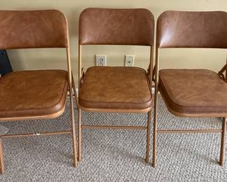 This lot features a set of three vintage Samsonite folding chairs, model number 3314, manufactured in March 1983. The chairs are upholstered in a durable, brown faux leather material with a slightly textured finish, reminiscent of aged leather. The frames are constructed from metal, likely steel, with a painted finish that appears to be a light bronze or gold hue. The design is classic for mid-century to late 20th-century folding furniture, prioritizing portability and storage. Each chair has a padded seat and backrest, offering a degree of comfort. The overall aesthetic suggests a practical and functional piece of furniture, typical of Samsonite's offerings during that era.