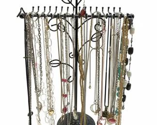 This collection features a variety of fashion necklaces, including delicate chains, beaded strands, and pendants. The display tree itself is a black metal, rose-themed stand designed to hold multiple necklaces, earrings, and bracelets. The necklaces appear to be made from various base metals, some with faux pearls, beads, and charms. Notable pieces include a large mother-of-pearl pendant and an oval locket with an ornate filigree design. The overall style leans towards costume jewelry, suitable for everyday wear or as part of a diverse accessory collection.