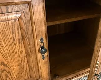 This large entertainment center armoire is constructed from solid oak, featuring a warm, medium-toned finish that highlights the natural grain of the wood. The design incorporates a central open section designed to house a television, with a smaller shelf below for media components. The lower section features two paneled doors with traditional hardware, opening to reveal shelved storage. The overall style is transitional, blending elements of traditional craftsmanship with a functional design suitable for modern media setups. The piece exhibits sturdy construction with visible joinery, suggesting it is a well-made, durable furniture item.