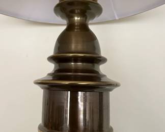 This is a Stiffel traditional table lamp featuring a metal base with an antique bronze or brushed nickel finish. The base has a tiered, decorative design with a bulbous body and stacked rings, culminating in a flared foot. It is topped with a classic bell-shaped fabric lampshade in a neutral beige or taupe hue, likely made of linen or a similar textile. The overall aesthetic suggests a classic or transitional style suitable for living rooms, bedrooms, or studies. The lamp appears to be in good condition, though some dust is visible on the shade and base.
