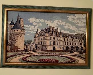 This framed tapestry depicts the Château de Chenonceau, a French Renaissance château spanning the River Cher. The artwork showcases intricate weaving techniques, capturing the architectural details of the château, its surrounding gardens, and a cloudy sky. The tapestry is housed in a decorative frame, likely intended for wall display. The label indicates it is part of a 'Tourist Scenes Collection' and measures 20x26 inches. Design number 7947.08.