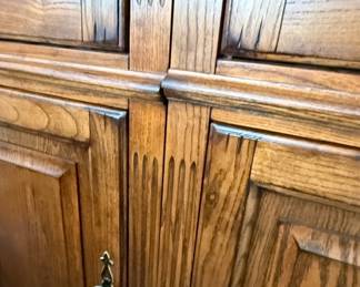 This vintage china cabinet is crafted from solid oak, featuring a warm, natural wood finish that highlights the grain patterns. The upper section is divided into two sections, each with a glass-paned door, allowing for display of china, glassware, or collectibles. The doors have decorative metal pulls and the frame is adorned with vertical fluted detailing. The lower section consists of two paneled wooden doors, providing concealed storage. The overall style suggests a traditional or farmhouse aesthetic, likely dating from the mid to late 20th century. Based on historical sales data, this piece is likely from Drexel Furniture.