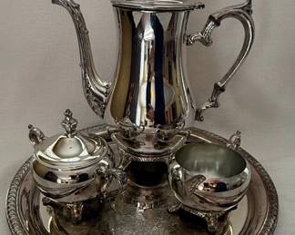 This elegant four-piece silver-plated set, manufactured by the International Silver Company, includes a coffee pot, teapot, sugar bowl with lid, creamer, and a decorative tray. The pieces feature a classic design with ornate handles and feet, and the tray has a detailed embossed pattern within a rope-twist border. The coffee pot and teapot have finials on their lids, adding to their decorative appeal. The overall finish is highly reflective, characteristic of polished silver plate. The set appears to be in good condition with minor signs of age and use, consistent with its vintage nature.